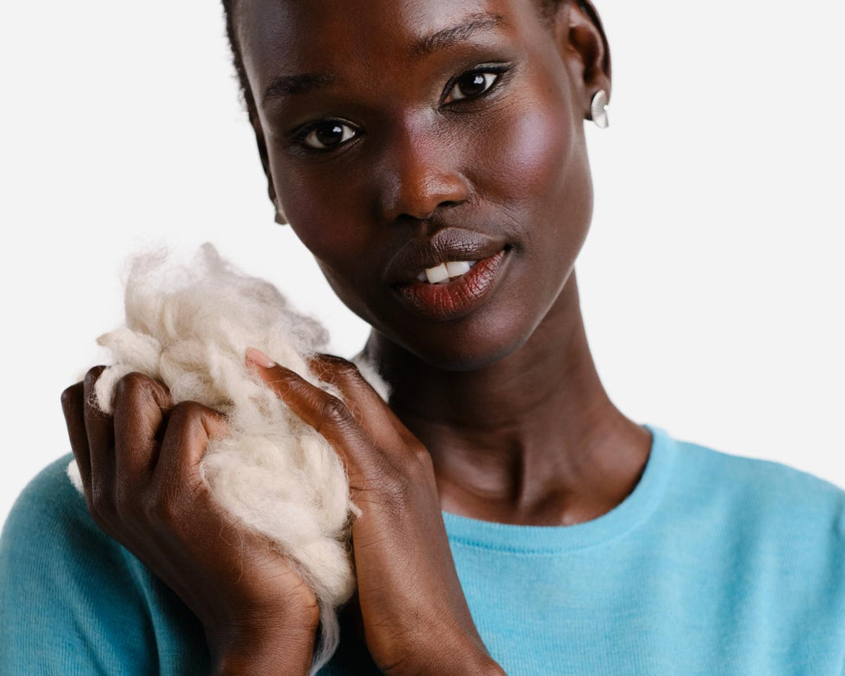 Model in a turquoise alpaca T-shirt holding raw alpaca fibre